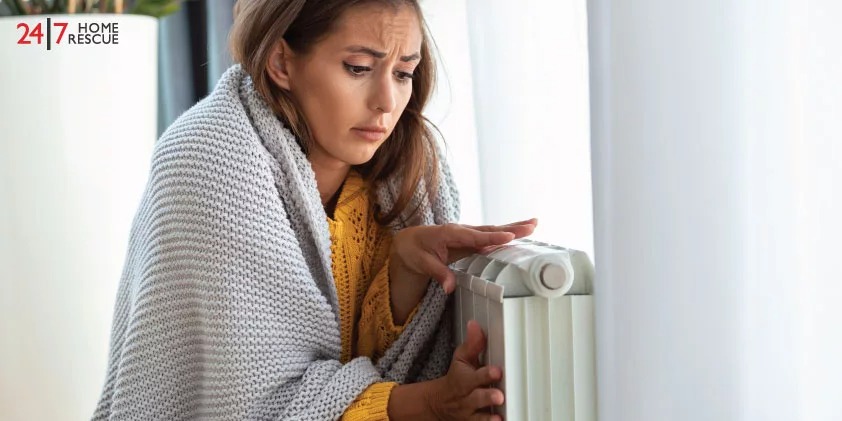 A person wrapped in a blanket adjusting a radiator heater