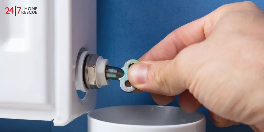 A person using a key to loosen the bleed valve of radiator