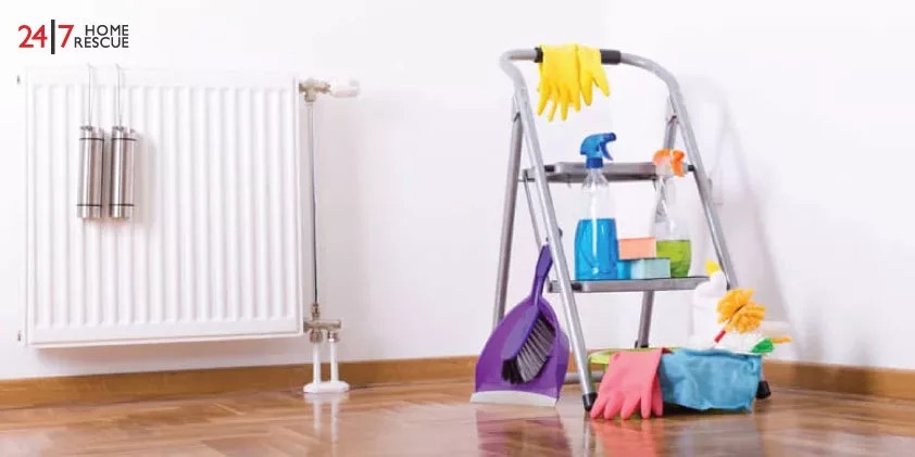 Cleaning supplies including a step ladder, gloves, and bottles of cleaning agents, positioned near a white radiator