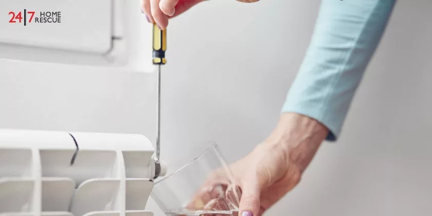 A person is using a screwdriver to bleed a radiator