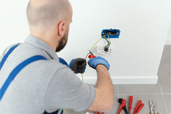 Electrician repairing electrical wires inside wall socket with tools on floor