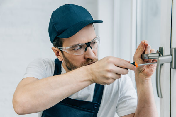 Locksmith in safety glasses repairing a door handle with a screwdriver.
