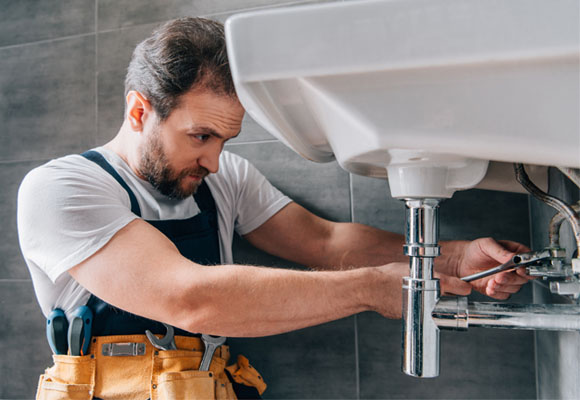 Plumber repairing a bathroom sink with tools and pipes exposed beneath the basin
