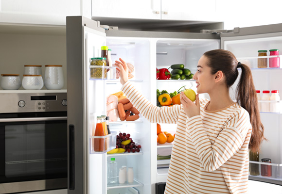 Woman choosing fruit from open fridge freezer – Fridge Freezer Insurance