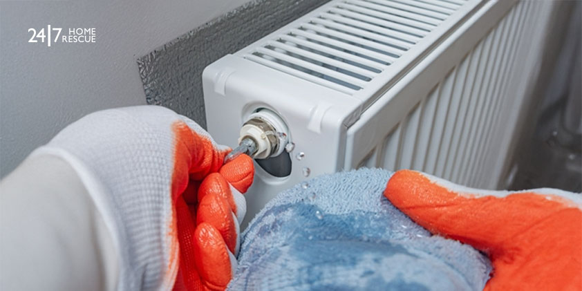 A person turns a radiator key to release air from a heating system valve