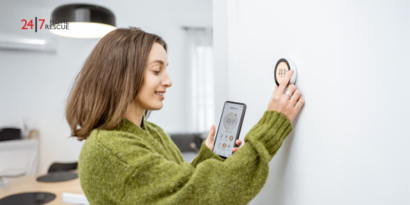 Woman in green sweater synchronizing a wireless thermostat with her smartphone